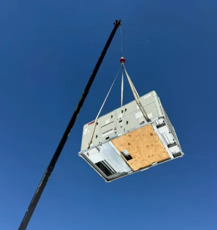 Crane lifting a large white modular structure against a clear blue sky