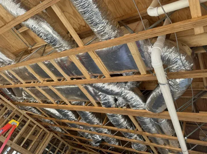 Exposed attic framing with silver ductwork and white PVC pipes overhead