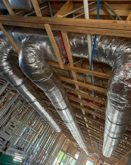 Insulated silver HVAC ducts running along exposed wooden ceiling framing under construction