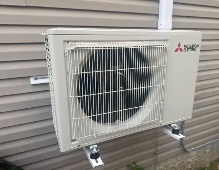 White Mitsubishi mini-split outdoor AC unit mounted on a house wall beside gray siding
