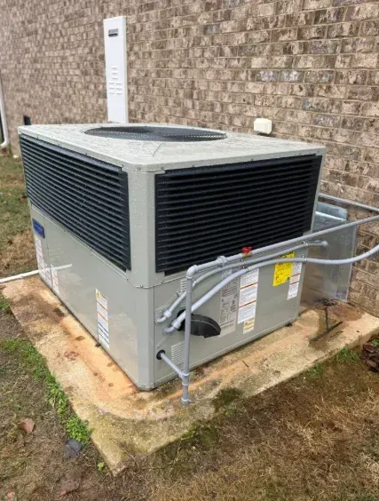Outdoor HVAC unit beside a brick wall, with gray panels and black vents on a concrete pad.