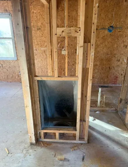 Unfinished wall framing with a metal fireplace insert in a room under construction.