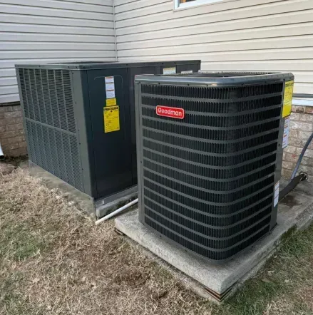 Two gray outdoor HVAC units on concrete pads beside a house with beige siding