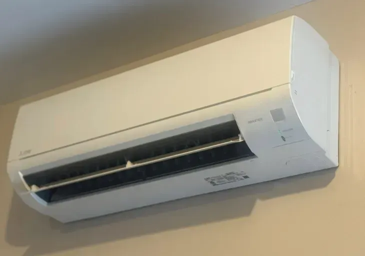 Wall-mounted white air conditioner on a beige wall, viewed at an angle
