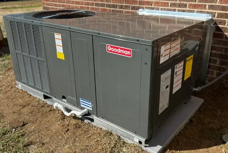 Gray Goodman rooftop HVAC unit on a gravel pad beside a brick building