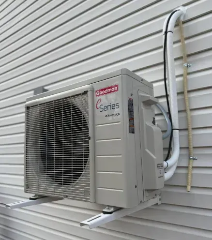 Wall-mounted outdoor air conditioner unit beside a house with white siding and visible refrigerant lines