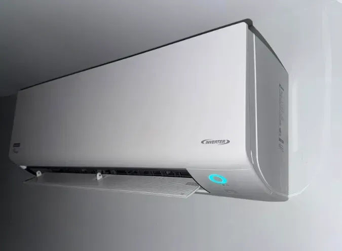White wall-mounted air conditioner unit on a light-colored wall, with blue indicator light on the right side.