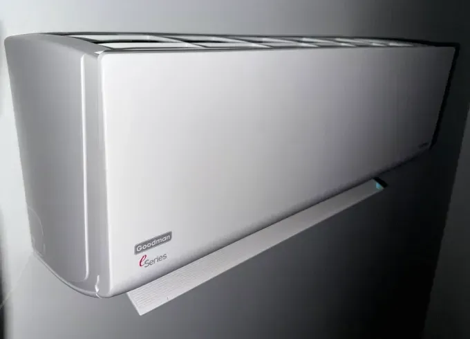 White wall-mounted air conditioner unit on a gray wall, with a small tilted support bracket beneath it