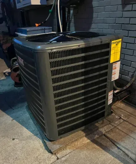 Outdoor gray air conditioner unit beside a brick wall on a concrete patio