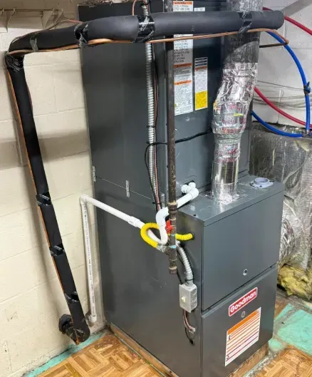 Gray HVAC furnace with connected ducts, pipes, and a yellow gas shutoff valve in a utility room