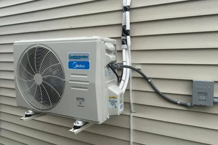Outdoor Mitsubishi mini-split air conditioner unit mounted on beige house siding with connected electrical box
