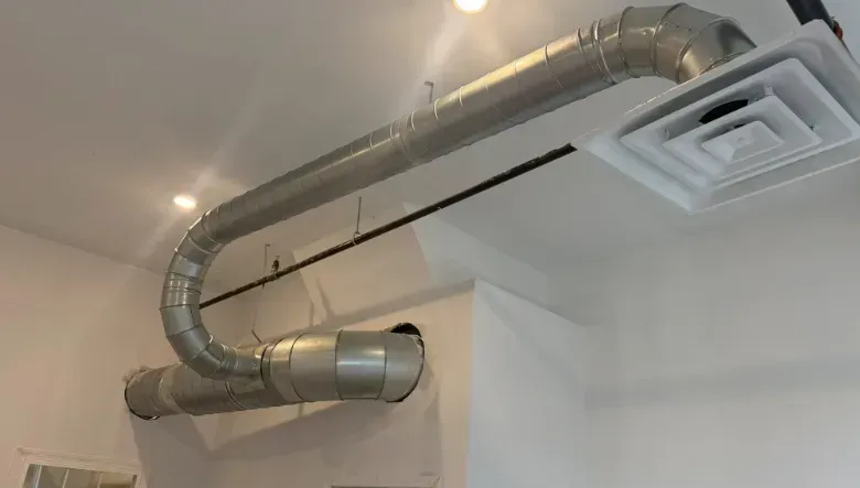Metal HVAC ducting and a ceiling vent running across a white room ceiling