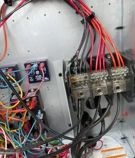 Electrical panel with dense red, black, and blue wiring connected to breaker blocks and relays.