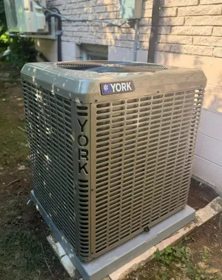 York rooftop air conditioner unit beside a brick house and bushes.