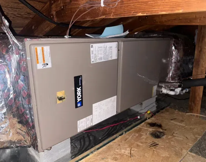 Rheem HVAC air handler in an attic, with exposed ductwork and insulation around it