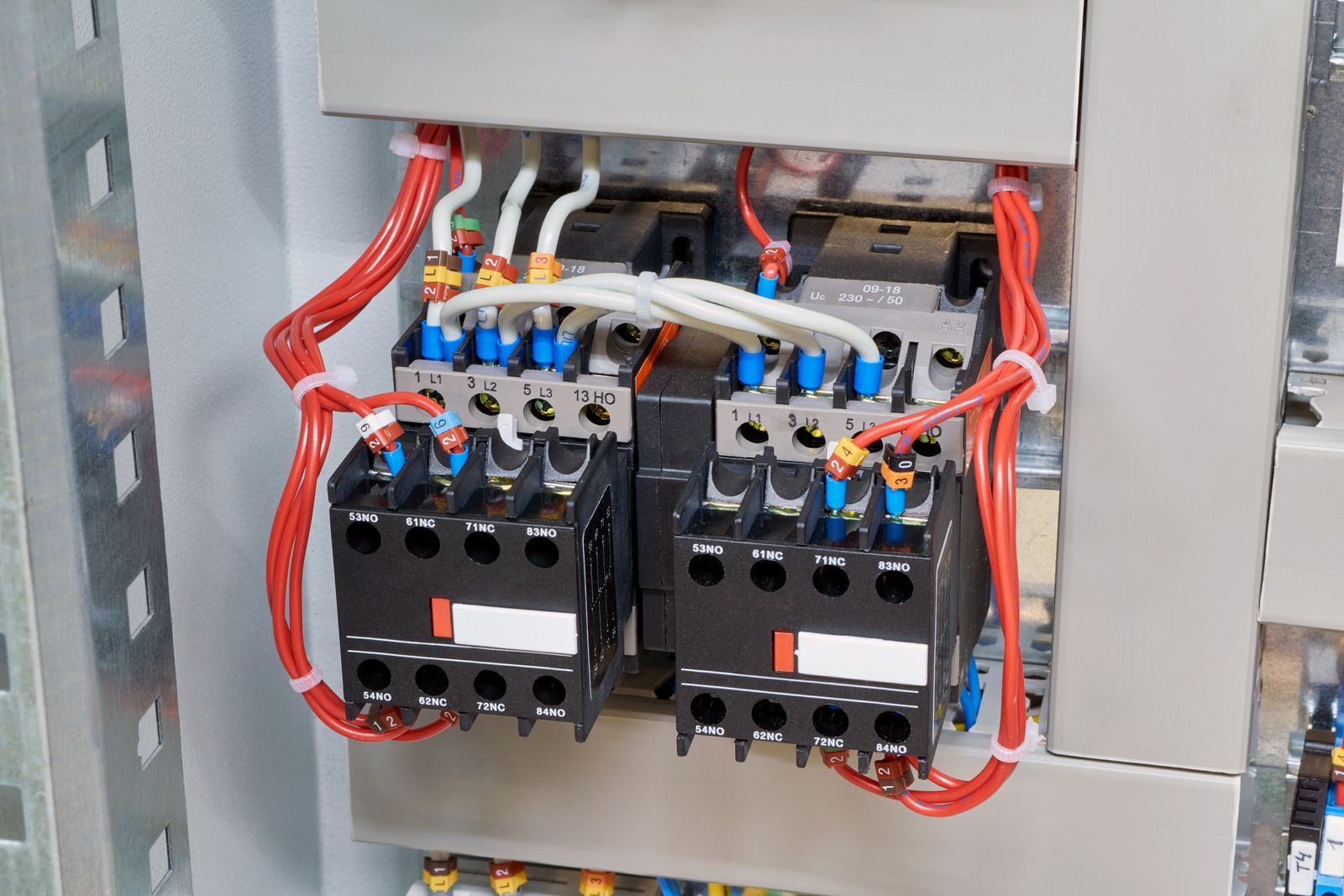 Electrical control panel with two black contactors, blue wiring, and red cables inside a metal enclosure