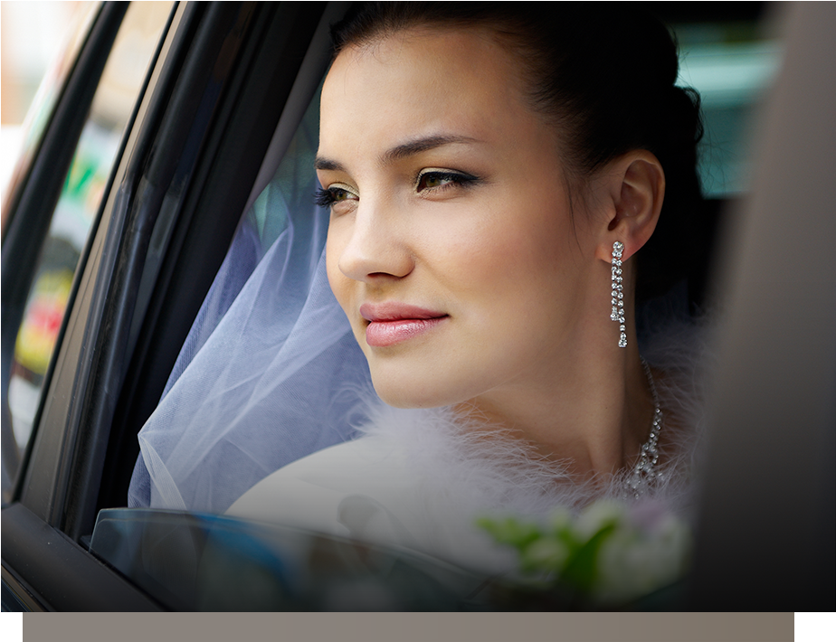 Bride in a white veil looking out a car window, wearing sparkling earrings.