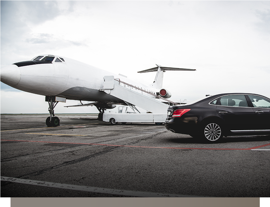 White private jet on tarmac beside a black sedan, with boarding stairs extended under a gray sky.