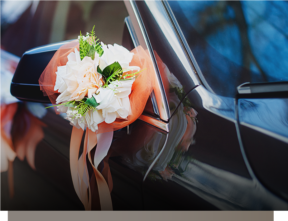 Wedding bouquet tied to a black car side mirror, with peach, white, and green flowers and ribbons.