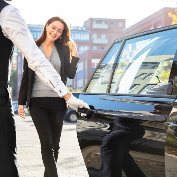 Woman smiling as another person opens the black car door on a city street