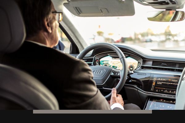 Driver seen from behind holding the wheel of a modern car interior on a sunny road
