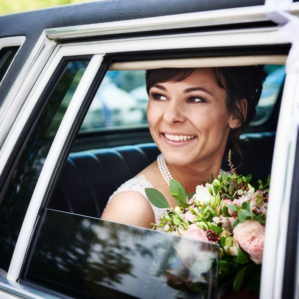 Smiling woman in a car holding a bouquet of flowers, looking out the window