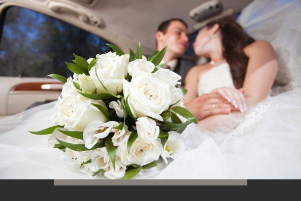 White bridal bouquet in foreground, with a blurred bride and groom kissing in a car background