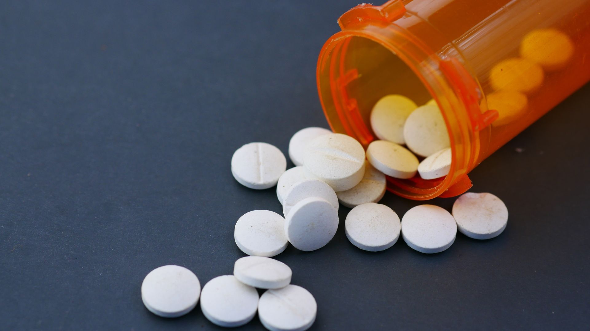 Orange pill bottle spilling white tablets on a dark surface