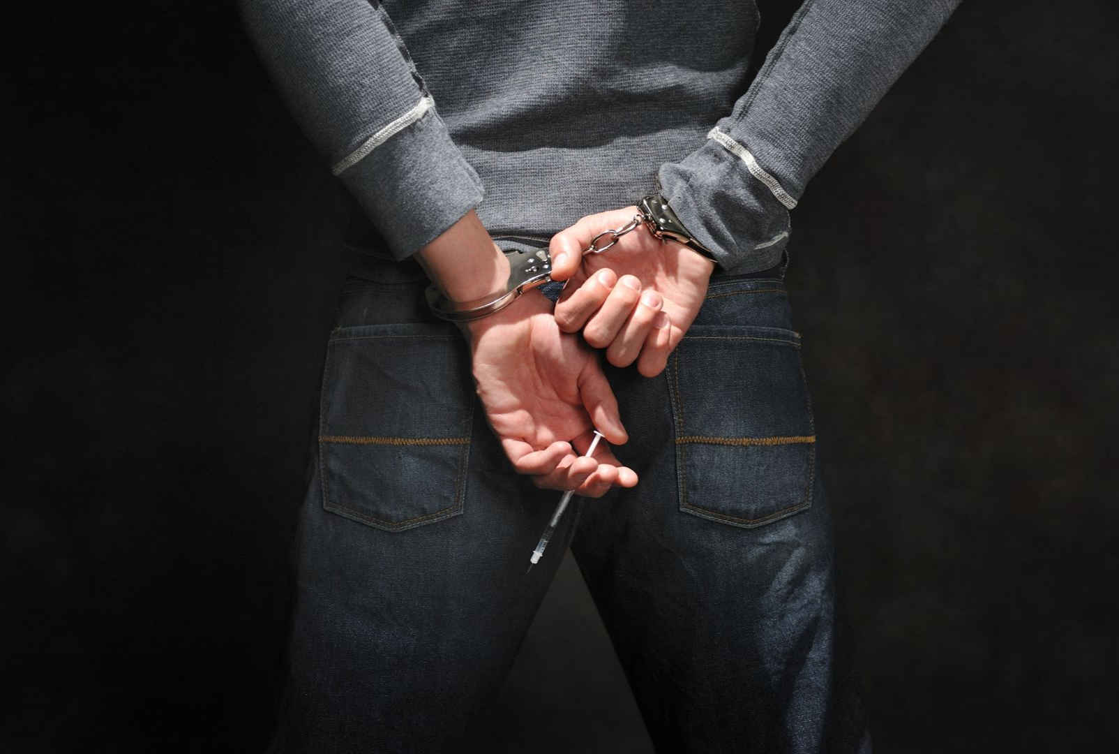 Person in handcuffs standing with hands behind their back against a dark background