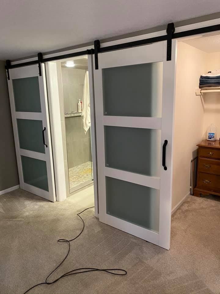 Open white sliding barn doors with frosted glass panels, revealing a doorway in a carpeted room.