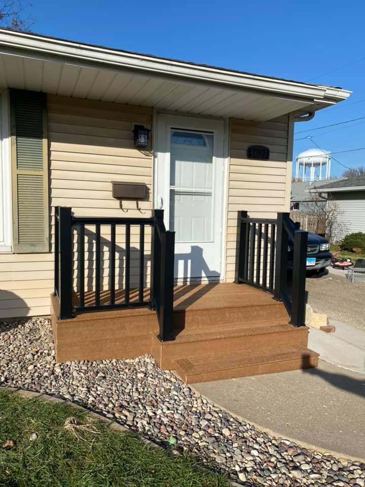 Small beige house entry with wooden porch steps, black railings, and a white door.