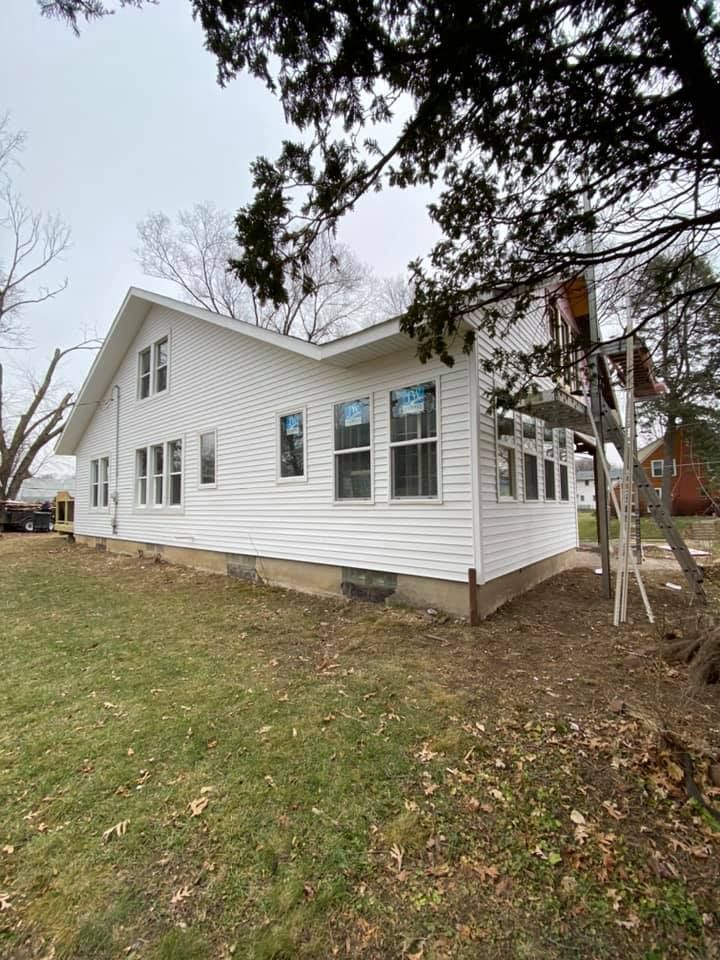 White house exterior with white siding, multiple windows, and a sloped roof on a grassy lot with trees nearby