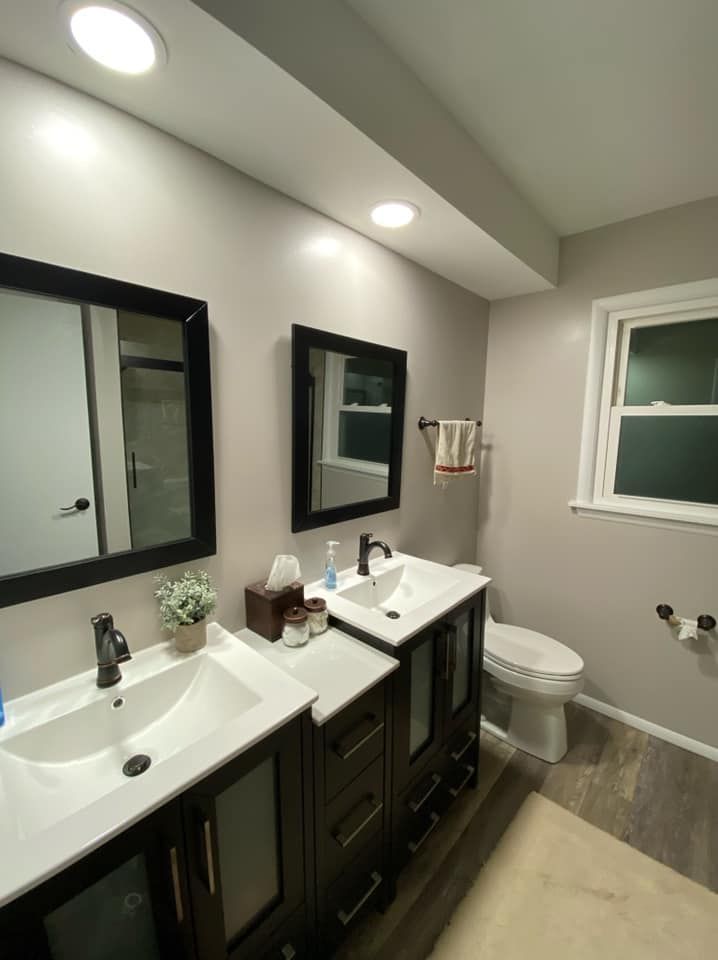 Bright modern bathroom with double sink vanity, mirror, toilet, and window.