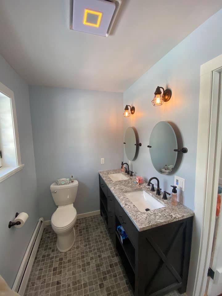 Small bathroom with toilet, dark vanity, twin mirrors, wall sconces, and a ceiling vent light.