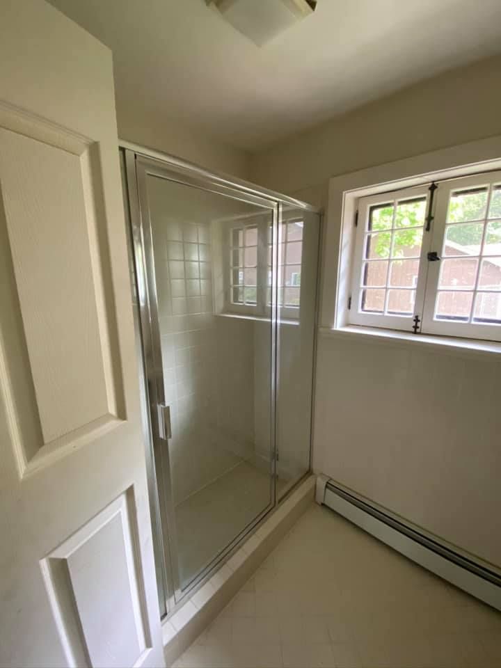 Bathroom with glass shower stall, window, and white walls