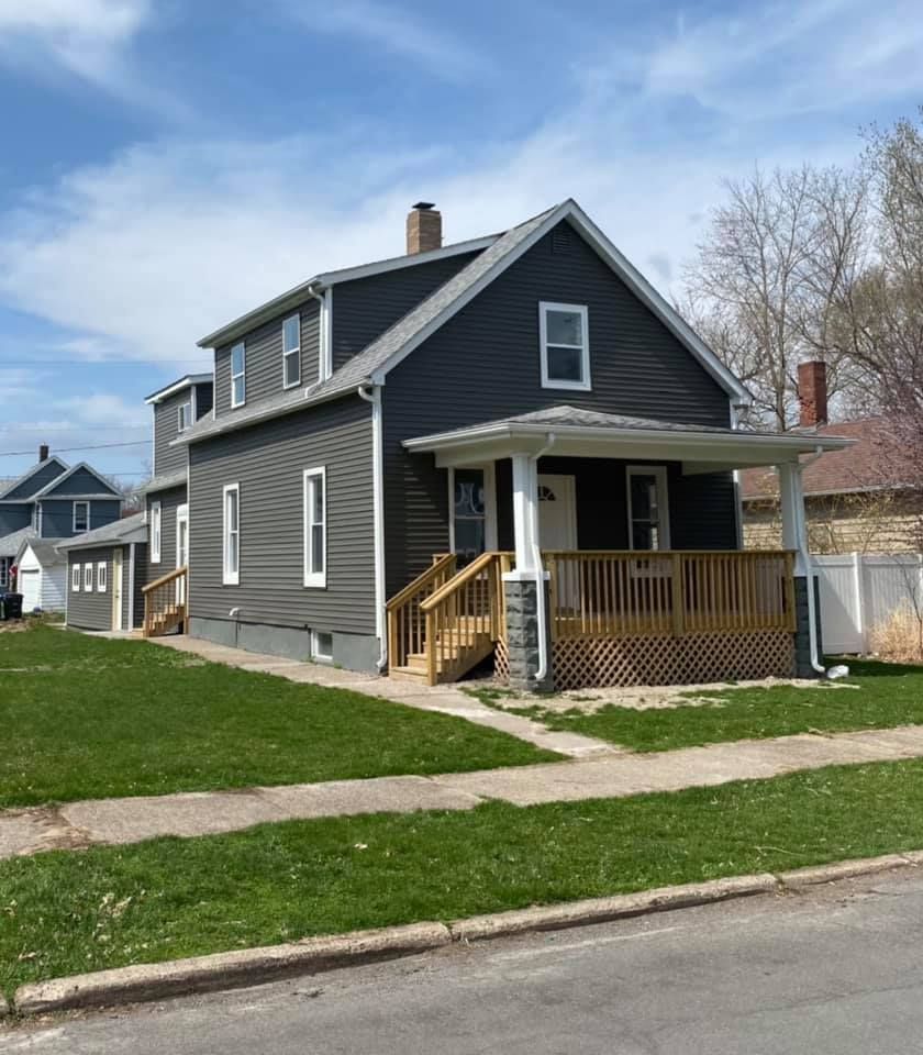 Dark gray two-story house with a front porch, white trim, and a green lawn beside a residential street.