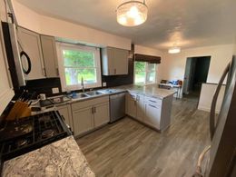 Modern kitchen with gray cabinets, island, wood floors, and a dining area in the background.