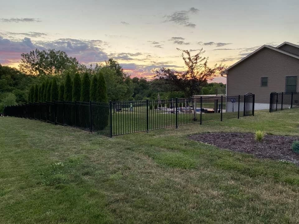 Fenced backyard with grass, a house, and a colorful sunset sky at dusk.