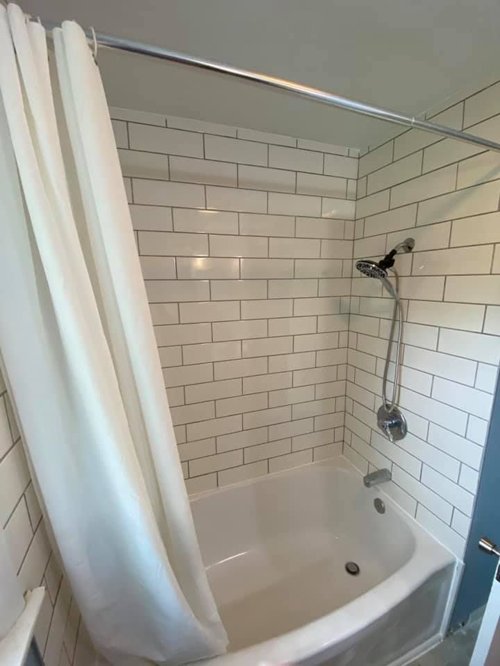 Small white-tiled bathroom with a bathtub, shower curtain, and wall-mounted showerhead