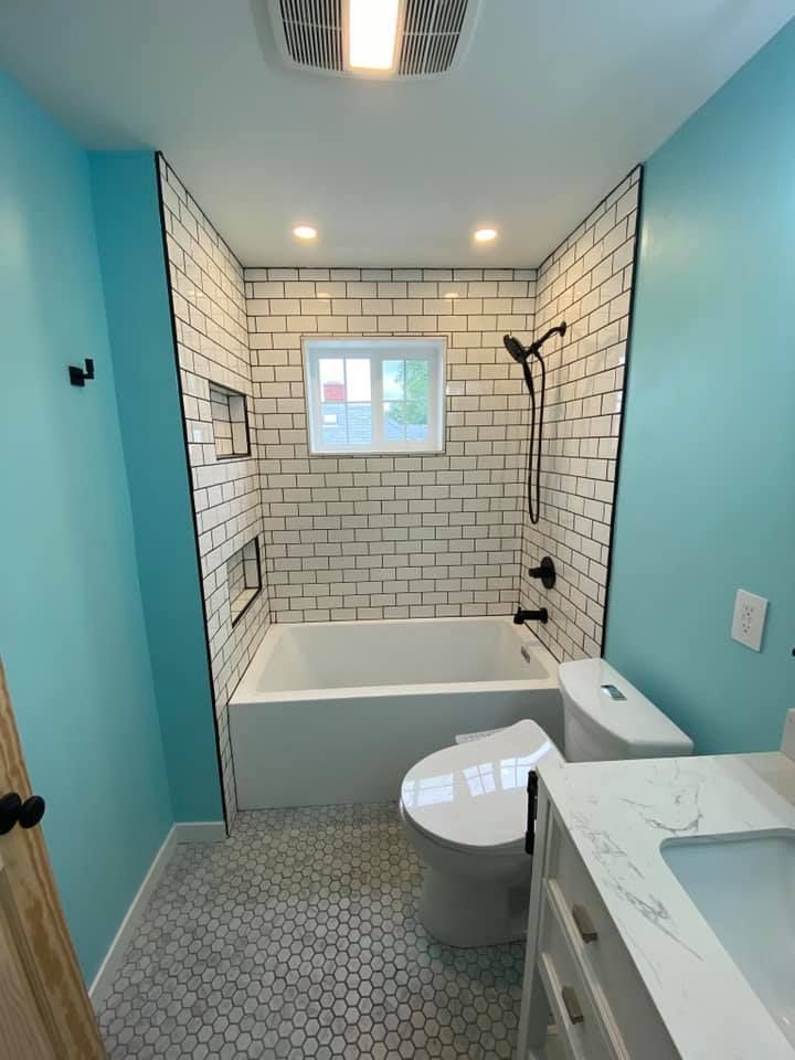 Bright blue bathroom with white subway tile shower, bathtub, vanity, and toilet under recessed lights
