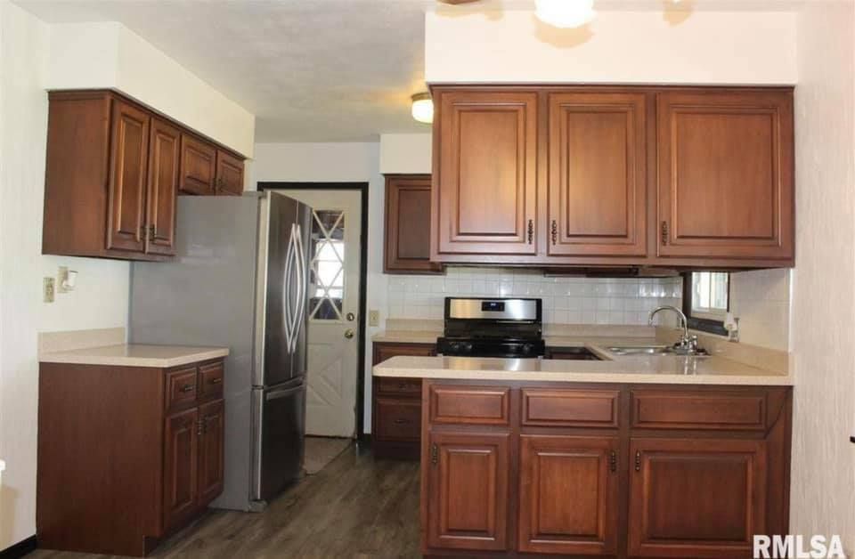 Small kitchen with brown wood cabinets, stainless refrigerator, black appliances, and light countertops.