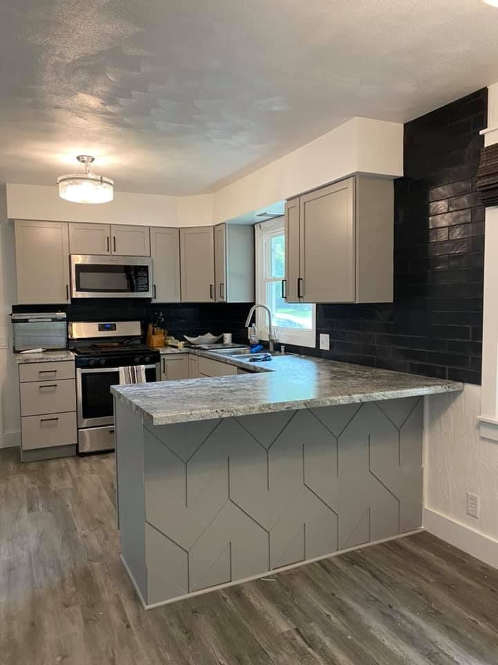 Modern kitchen with gray cabinets, black tile backsplash, and a white island with patterned front panel.