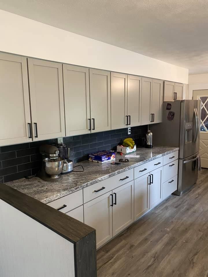 Modern kitchen with white cabinets, granite countertop, stainless steel fridge, and wood flooring.