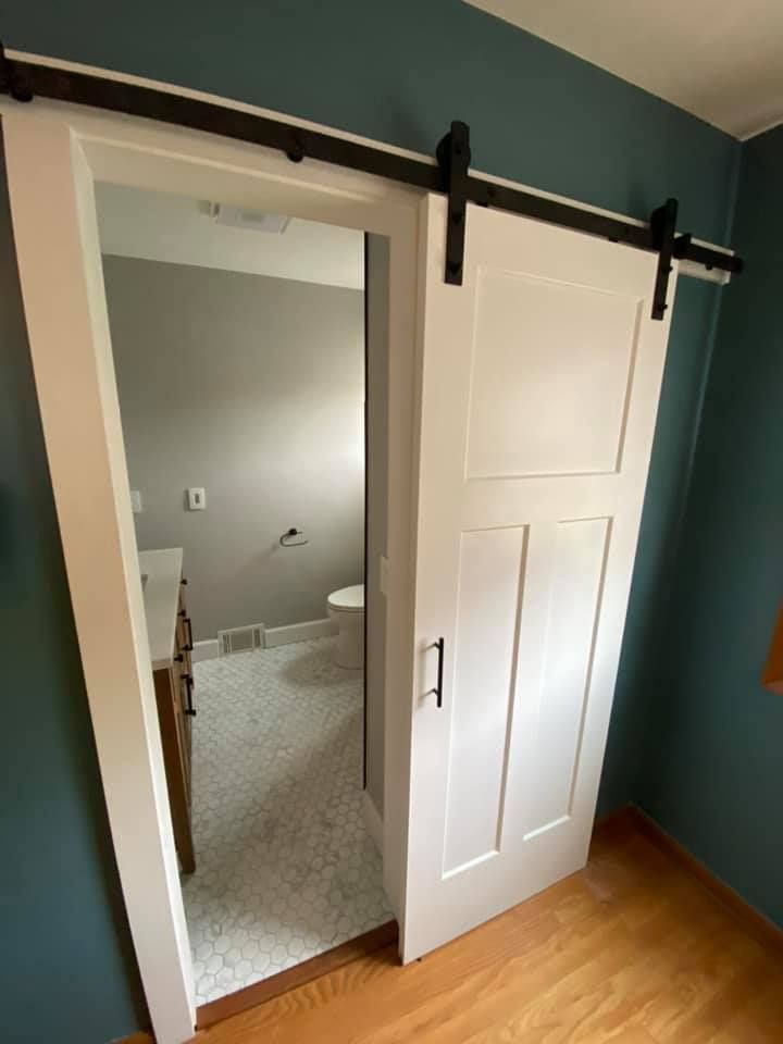 White barn-style sliding door partially open to a carpeted bedroom with a bed and dresser.