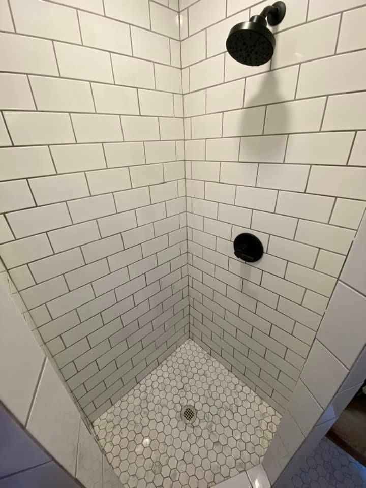 Empty white tiled shower stall with hexagon tile floor and dark shower fixtures, viewed from the corner