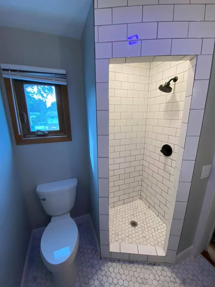 Small bathroom with toilet beside a tiled shower stall and blue window light.