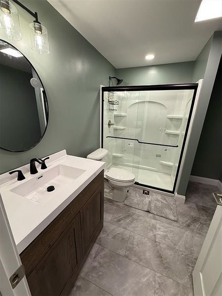 Modern bathroom with gray tile, white vanity, and glass walk-in shower