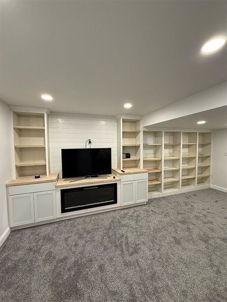Living room with built-in white shelving, TV, and gray carpeted floor