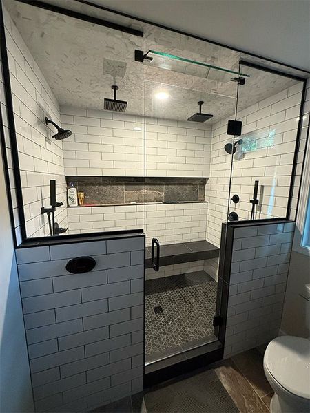 Modern black-and-white tiled shower with glass door and built-in bench in a bathroom