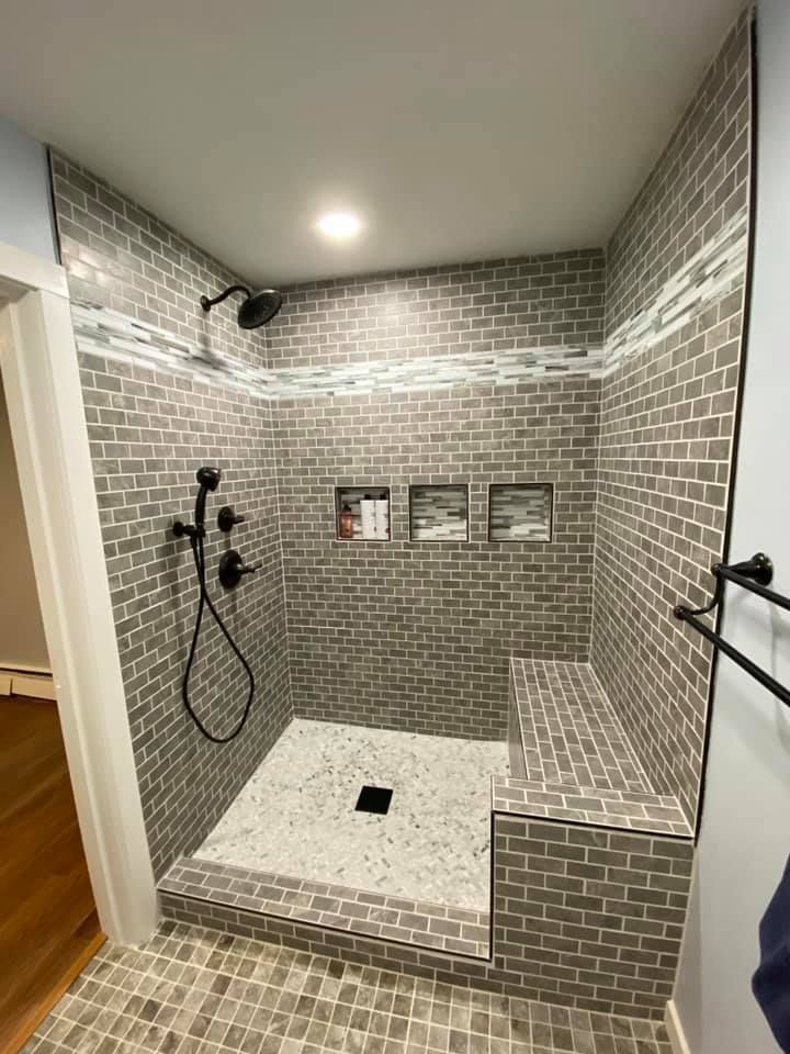 Gray-tiled walk-in shower with bench, black fixtures, and three wall niches under a ceiling light